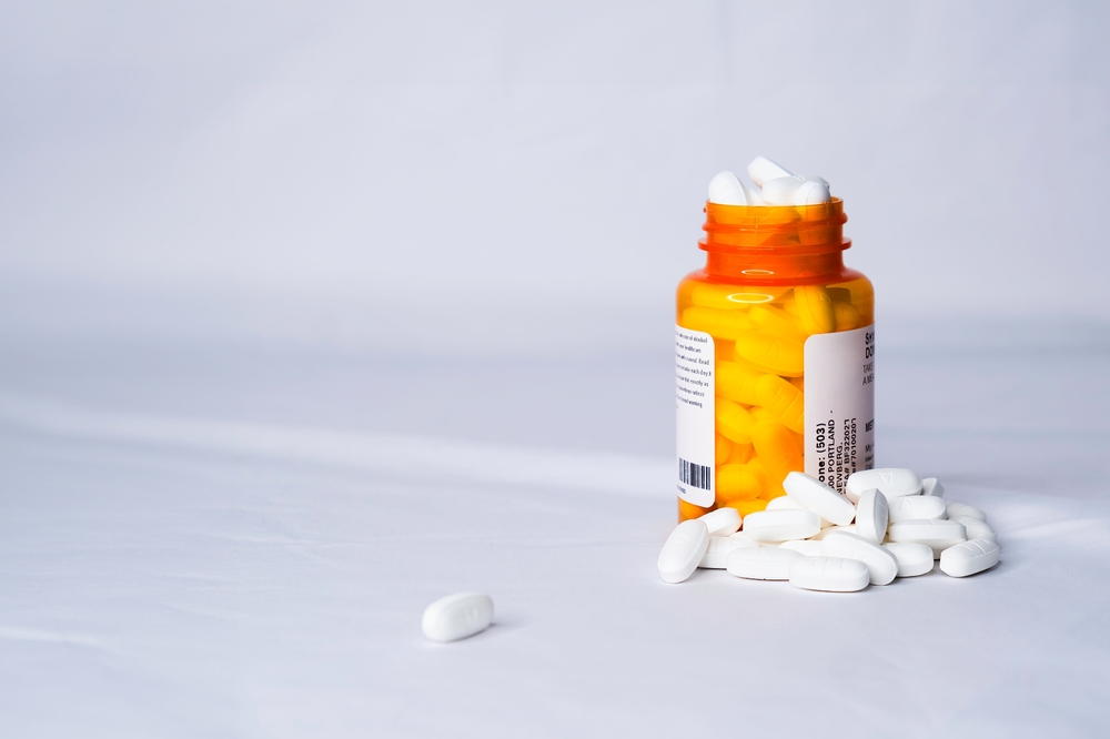 A single, orange prescription bottle overflowing with white medicine pills.