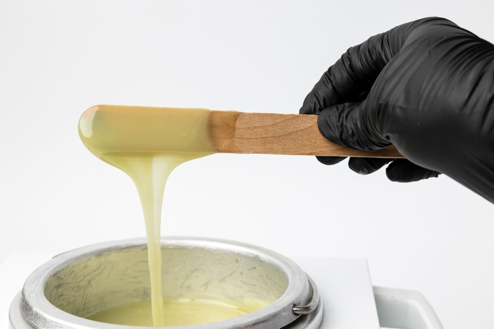 A human hand holding wooden sticks with wax over wax melter
