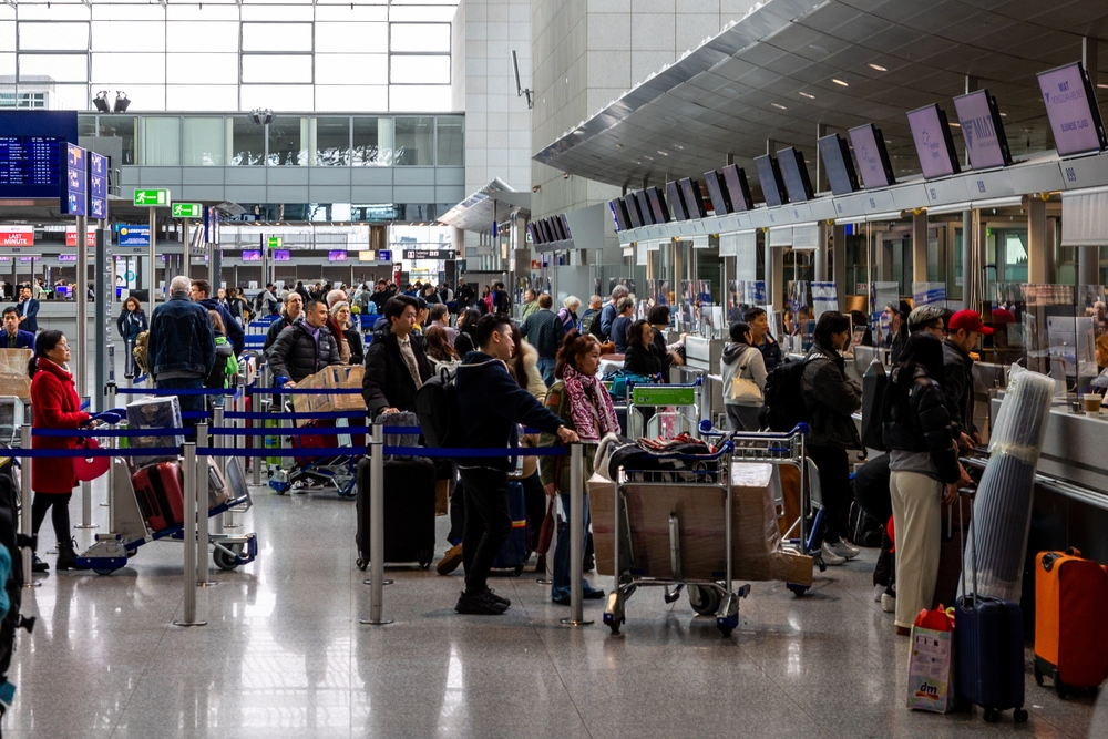 Frankfurt Airport, Germany - February 19, 2024: the image depicts a bustling airport check-in counter with numerous travelers waiting in line, pushing luggage carts, and interacting with airline staff