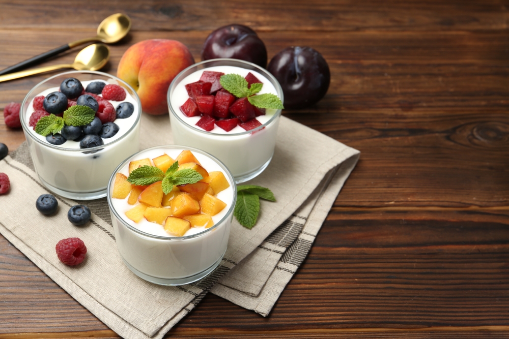 Tasty yogurt with fresh berries, fruits and mint in glasses on wooden table, closeup. Space for text