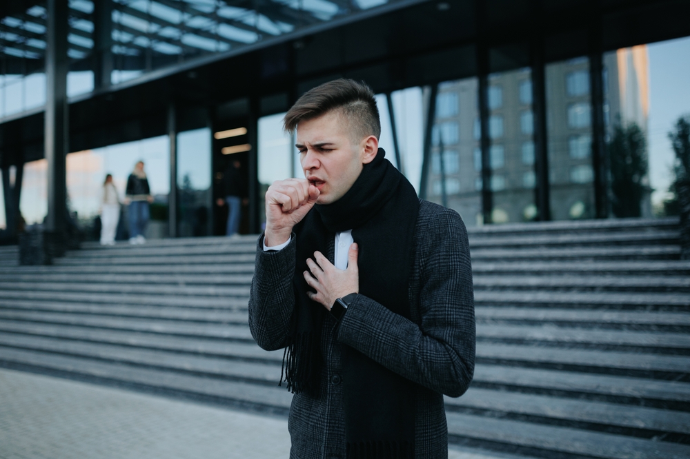 Suffering in the City A young man battles the flu with persistent sneezing and coughing, visibly distressed by the seasonal illness while outdoors.