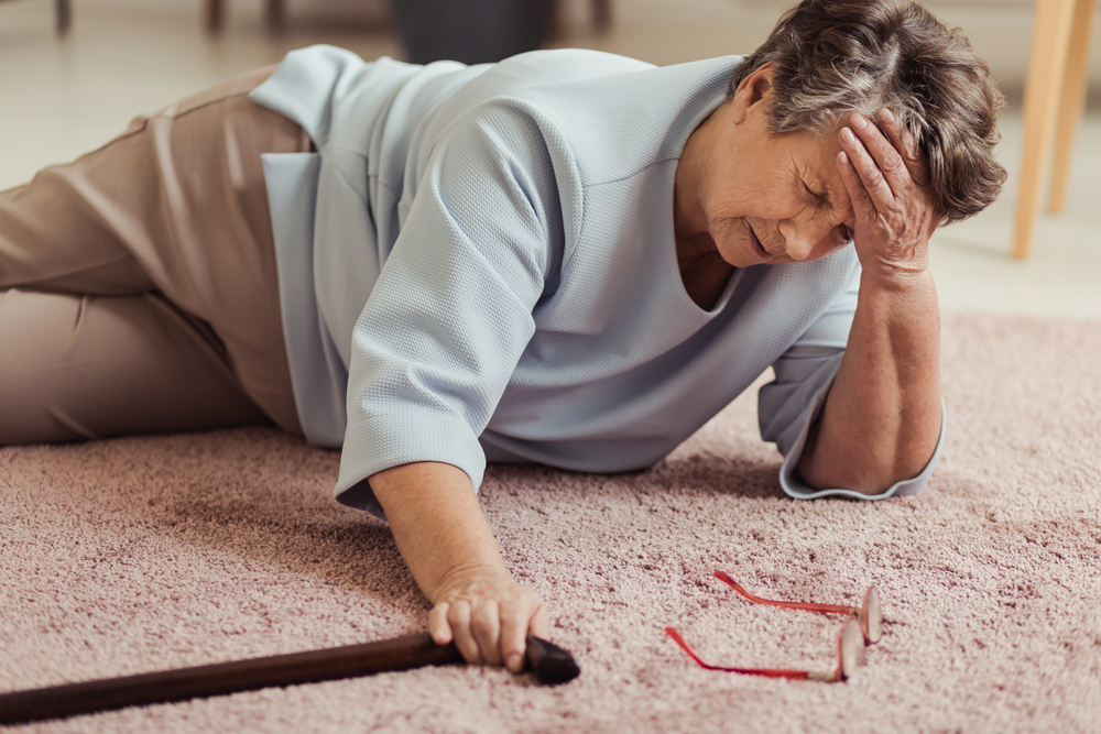 Sick senior woman with headache lying on the floor after falling down
