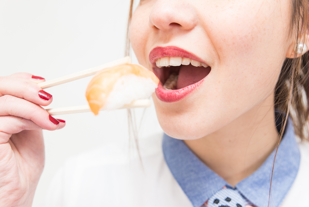 japanese woman eating sushi with salmon holding it with chopsticks. concept about, food, nutrition, sushi, restaurants, travel, and people
