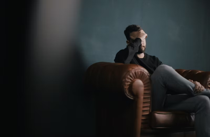 man sitting on a couch in the dark nursing a headache