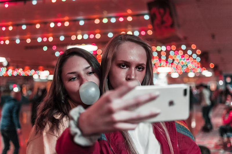 two girls taking a selfie with one blowing a bubble