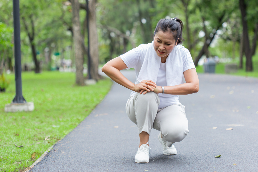 Asian elderly or senior woman accident falling down on floor in the park while running exercise have pain knee ache.
