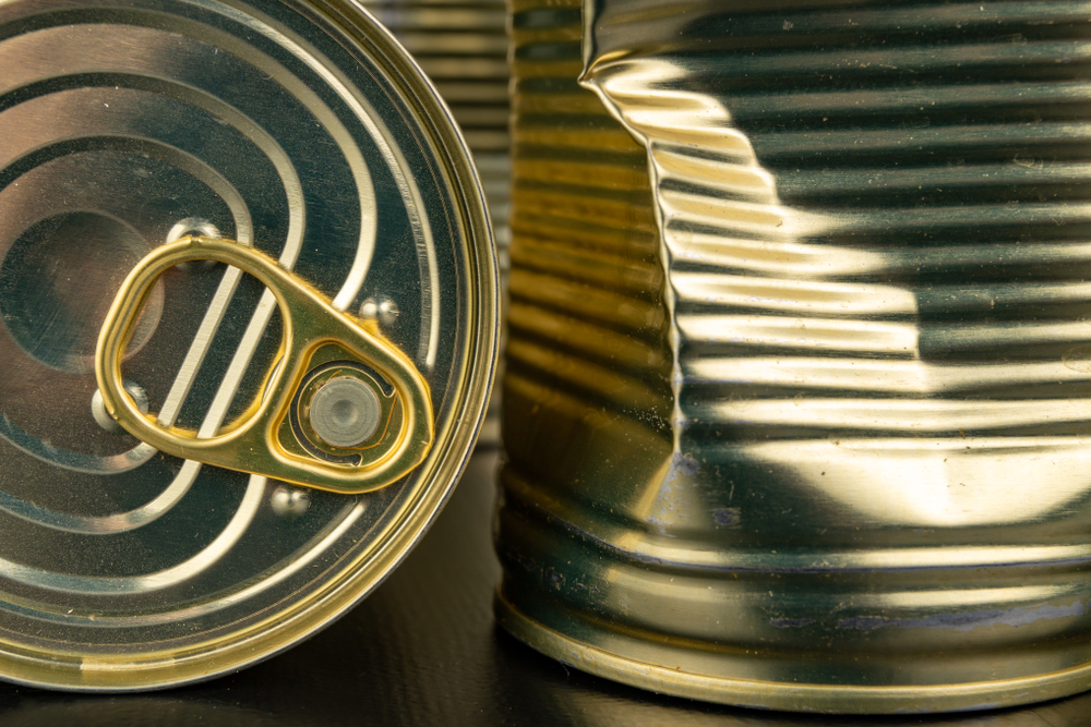 Damaged metal can with vegetables on a wooden table. Canned vegetables in a can. Dark background.
