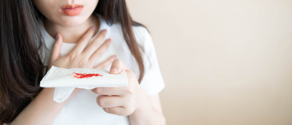 Woman have a coughing up blood and chest pain. Close up of hands holding tissue paper with bloody sputum. Cause of hemoptysis include TB, lung cancer, bronchitis, pneumonia or pulmonary embolism.