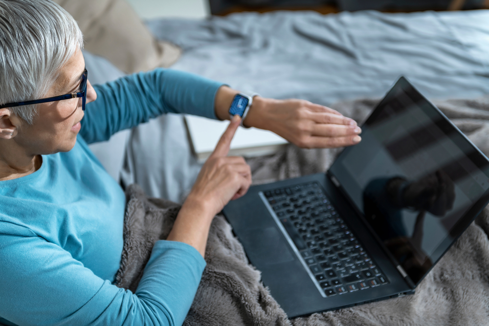 Orthosomnia – Unhealthy Interaction of Technology and Sleep - Woman with Smart Watch and Laptop in Bed, Concerned about Her Sleep Quality
