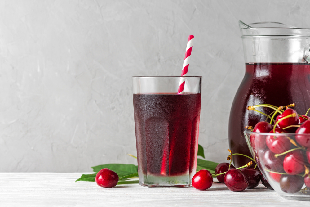 Cold cherry juice in a glass with a straw and jug with fresh berries on white background. Refreshment summer drink. Healthy drink