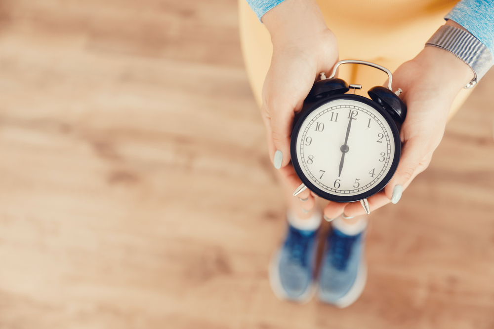 Healthy sleep concept top view. Girl in sportswear alarm clock six in morning for early rise to fitness workout.

