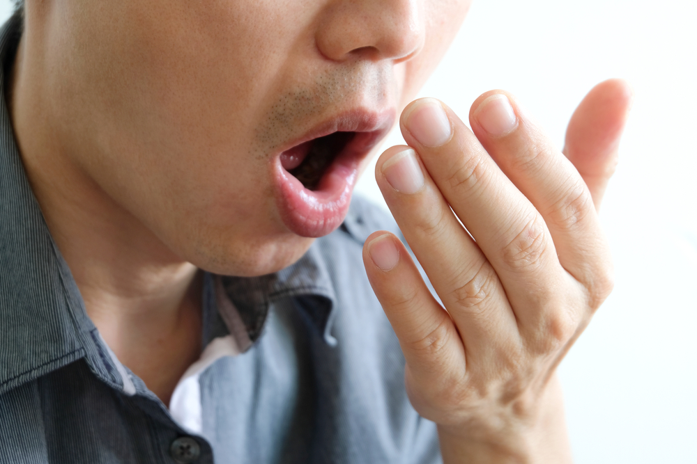 A man checks for bad breath and breathes with his hands. he has bad breath Concept of oral and dental health