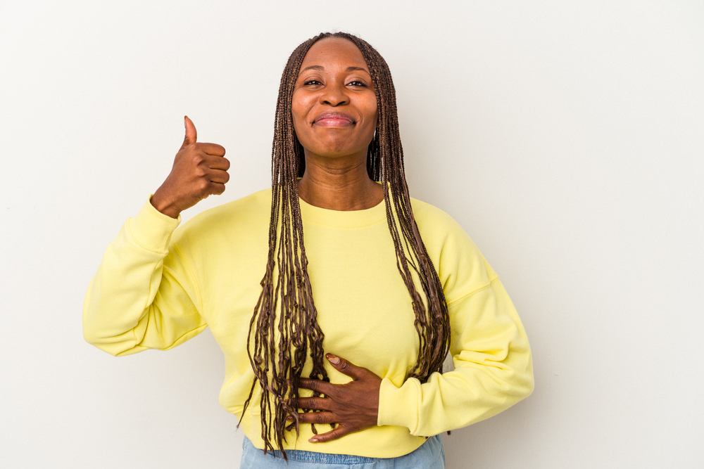 Young african american woman isolated on white background touches tummy, smiles gently, eating and satisfaction concept.

