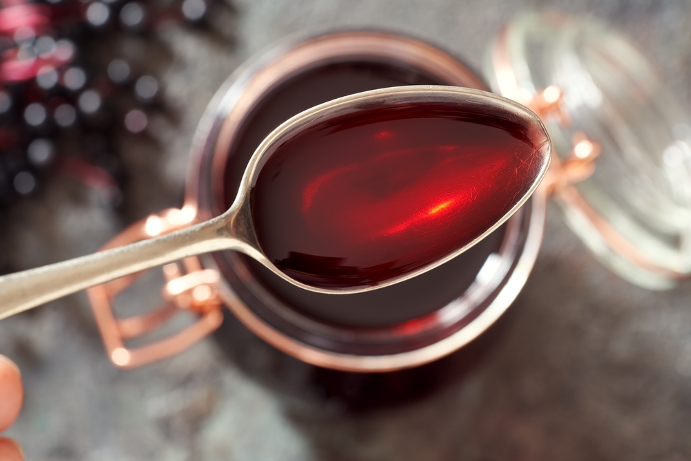 Black elder syrup with fresh elderberries in the background
