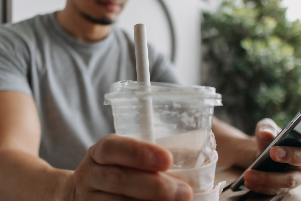 Close up of asian man use paper straw for his drink in the cafe.