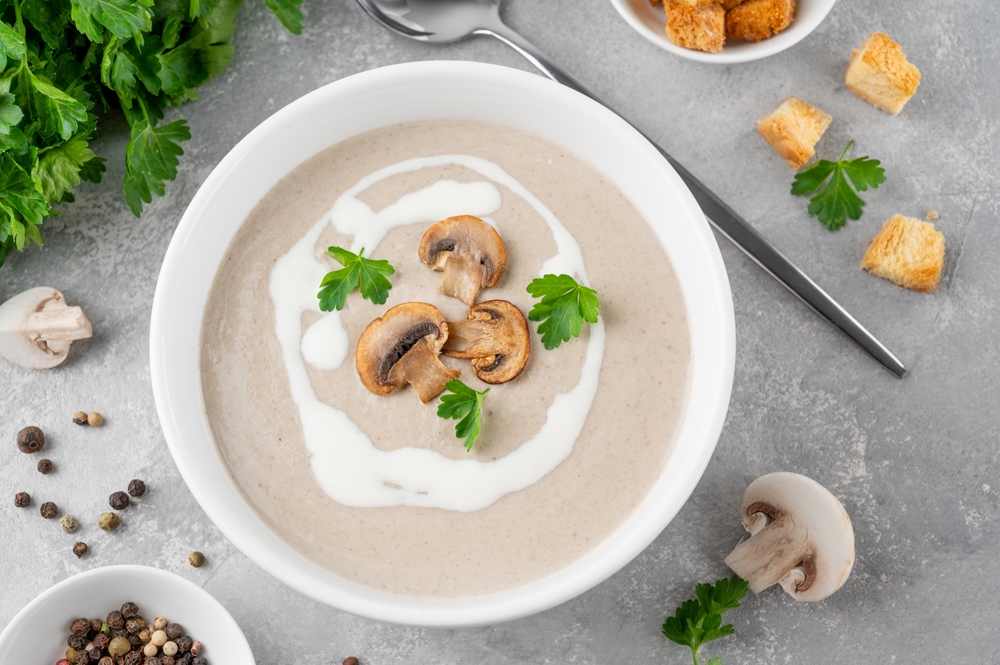 Mushroom cream soup with cream, croutons and herbs on a white wooden background. Delicious comfort food