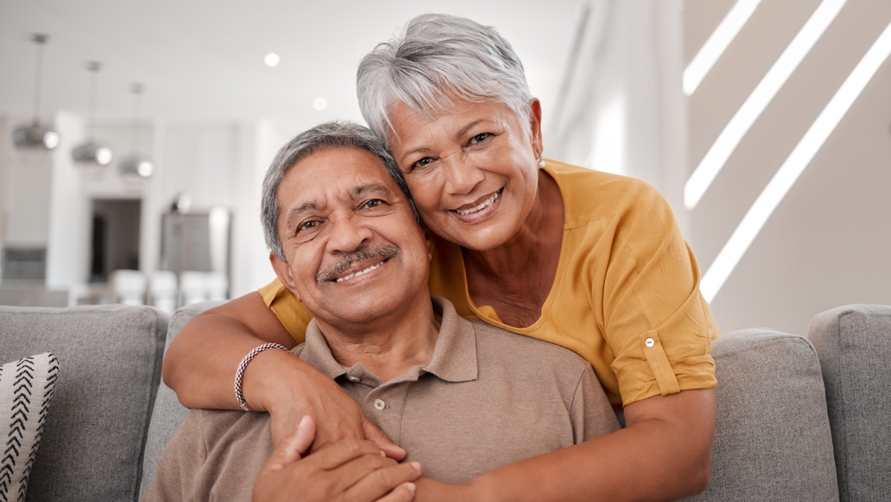 Portrait of elderly love, grandparents smile on sofa and old couple relax at home in happy retirement. Senior man, grandmother on couch and smile in living room getting hug from retired wife on couch
