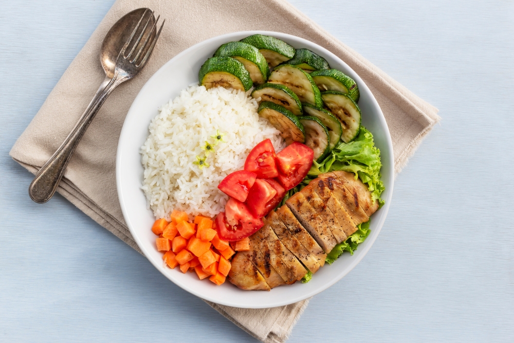 Grilled chicken has rice and zucchini carrot tomato in plate on wood background, top view, healthy food concept.