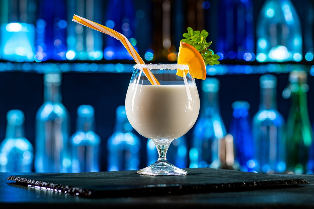 Cocktail Pina Colada on bar counter in a restaurant, pub. Fresh drink with rum, pineapple juice, coconut milk. Alcoholic cooler beverage at nightclub. Showcases with bottles on dark background.