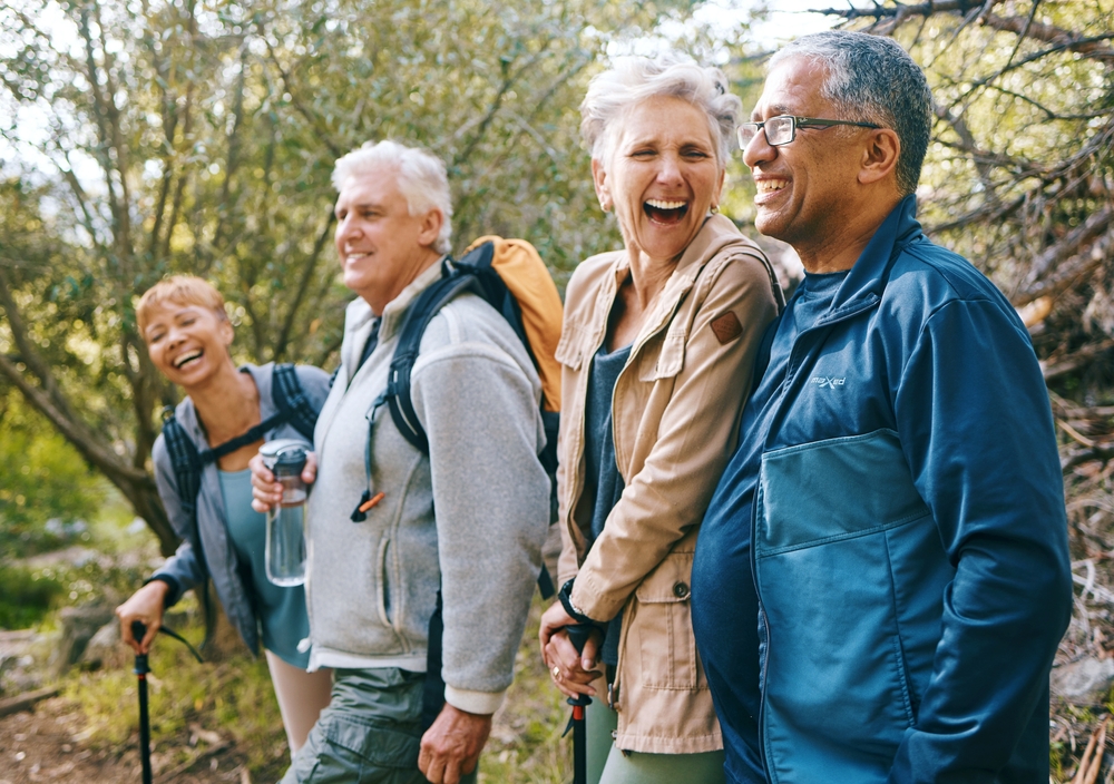 Nature, hiking and happy senior friends bonding, talking and laughing at comic joke in forest. Happiness, fun and group of elderly people trekking together for health, wellness and exercise in woods.

