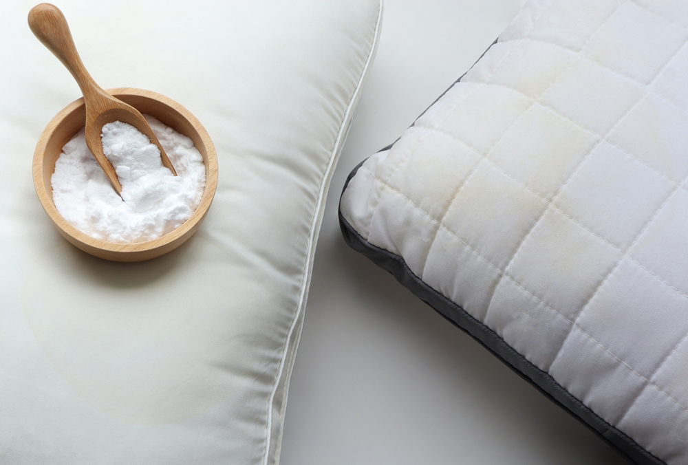 White pillow with yellow saliva stains and baking soda (sodium bicarbonate) on white background. baking soda to clean their dirty mattresses and Home cleaning concept.