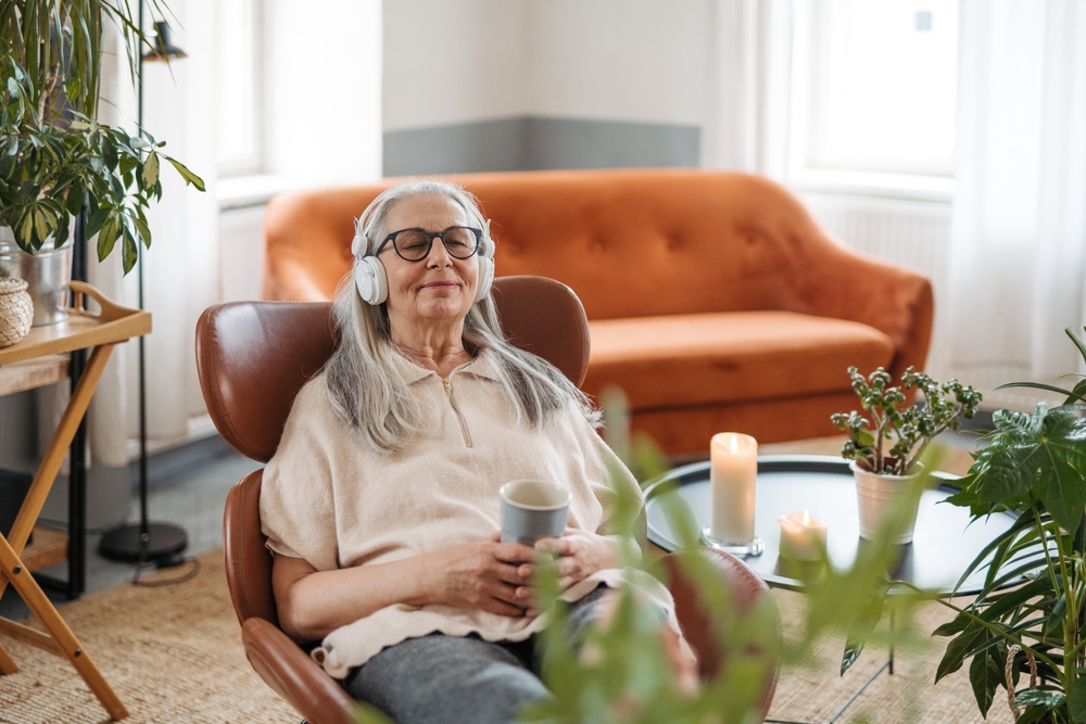 Senior woman resting with cup of tea in her living room, listening music.