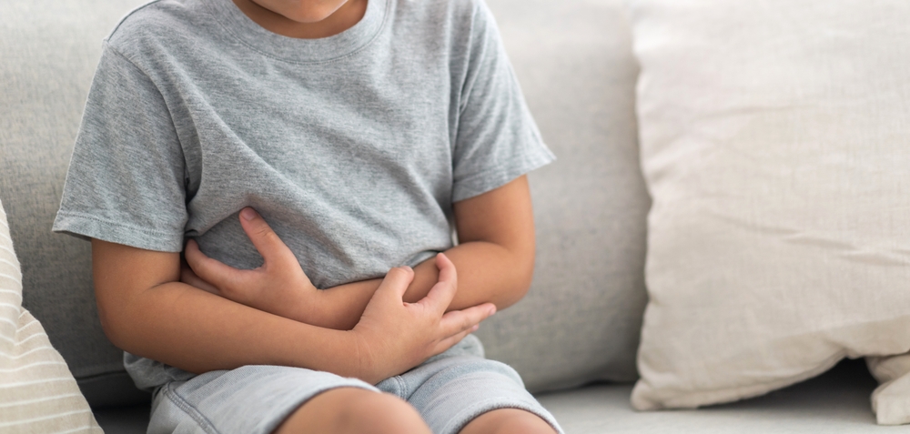 Portrait of sick unhappy little child asian boy touching belly stomach with suffering from stomach ache pain, gastritis at home
