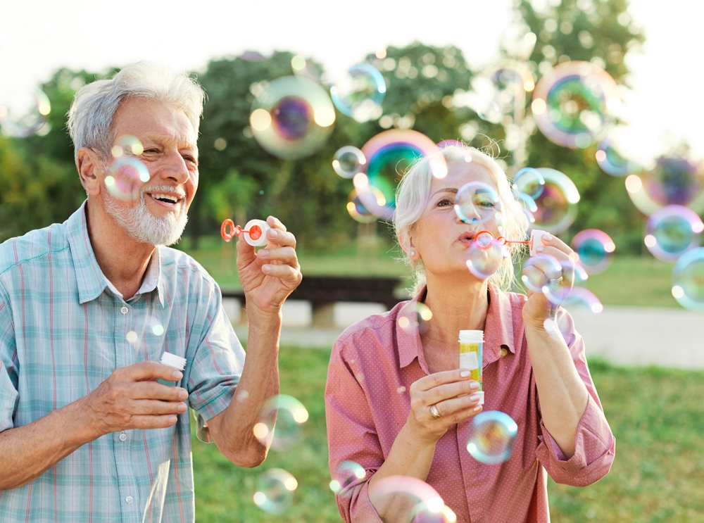 Happy active senior couple having fun blowing soap bubbles in park outdoors. Vitality and active senior couple concept
