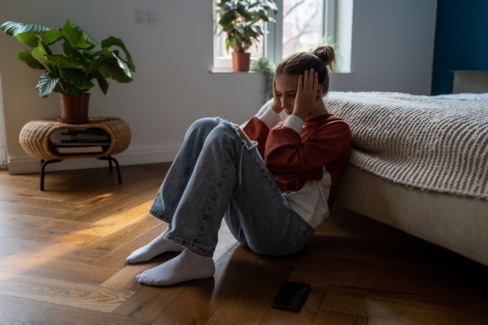 Frustrated sad teen girl child sitting alone on floor being bullied online, having feelings of isolation and fear. Depressed teenage kid holding head in hands dealing with first love heartbreak
