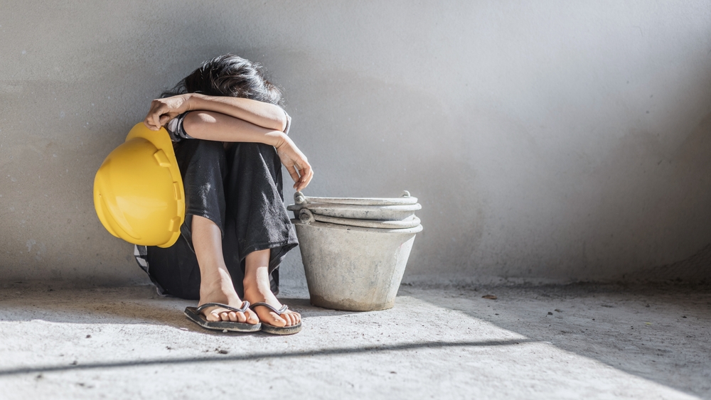 Sad child labor girl relaxing from construction work. World Day Against Child Labour concept.