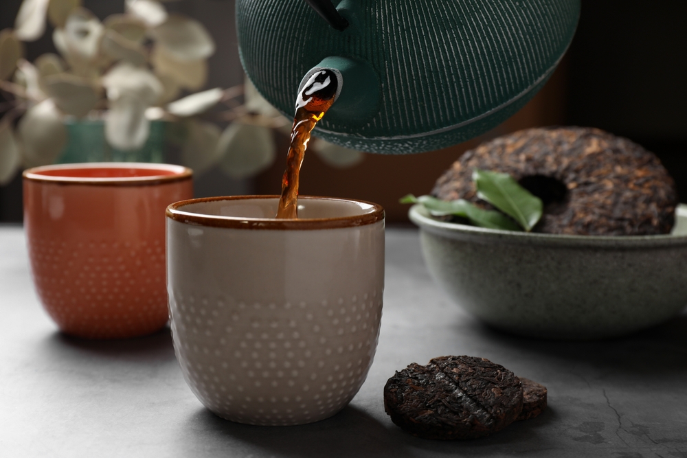 Pouring freshly brewed pu-erh tea into cup on grey table, closeup
