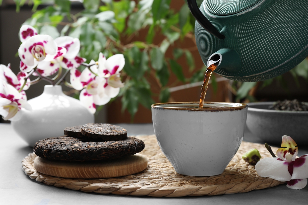 Pouring freshly brewed pu-erh tea into cup on grey table, closeup
