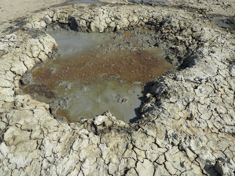 Crater with gray volcanic healing clay. A hole with a prominent amorphous mass from the depths of the earth. Mud and gas eruption. Temryuk, Russia. Cracked soil surface. Texture of a mudflow cracks
