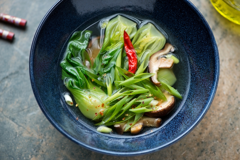Vegetable soup with bok choy and shiitake mushrooms in a dark-blue bowl, middle close-up, high angle view