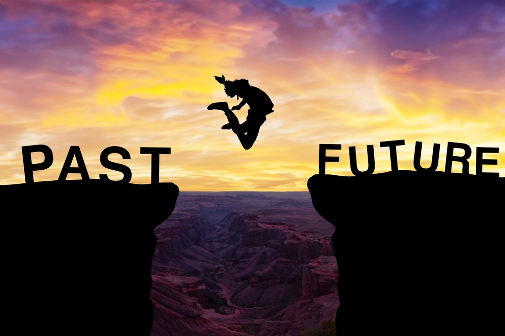 Silhouette of a person leaping between cliffs labeled 'PAST' and 'FUTURE'. Vibrant sunset illuminates a deep canyon below, symbolizing risk, growth, and change