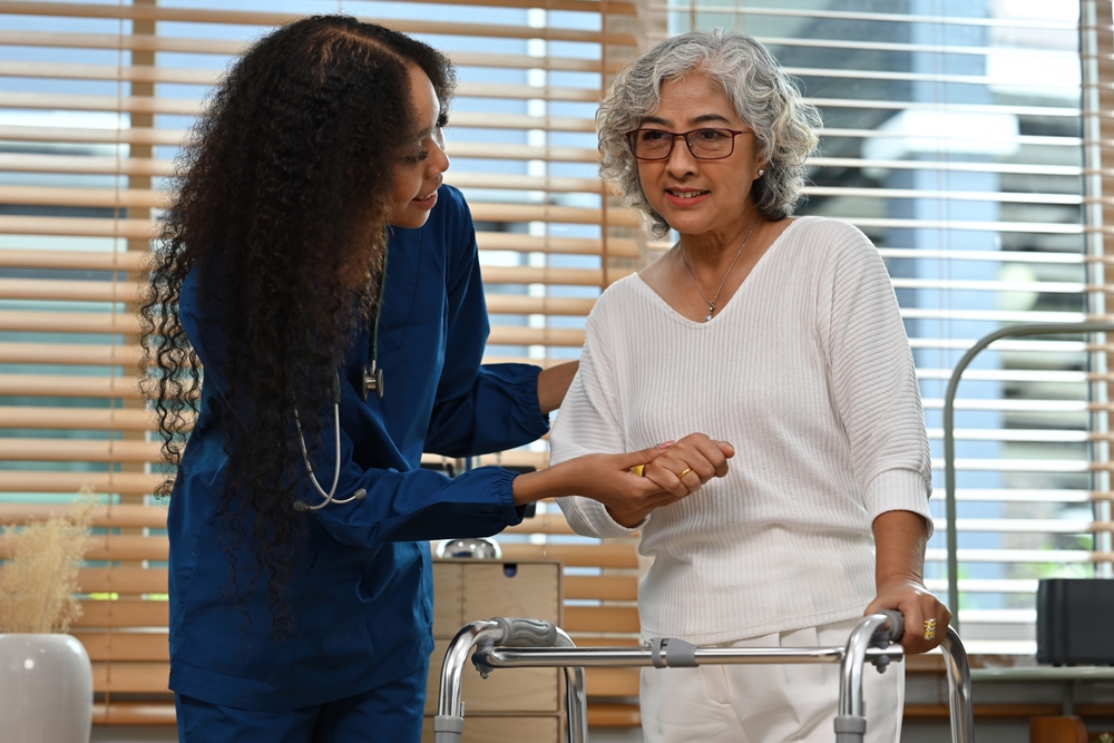 An African Physical therapist or Caregiver help and support the old stroke patient woman standing with a walker at home. A home exercise program after a stroke concept.