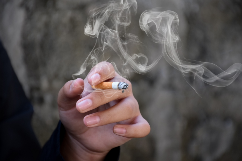 Closeup hand holding lighted cigarrette of asian smoking boy in private area of school and house to avoid punishment from teachers or parents, new edited.
