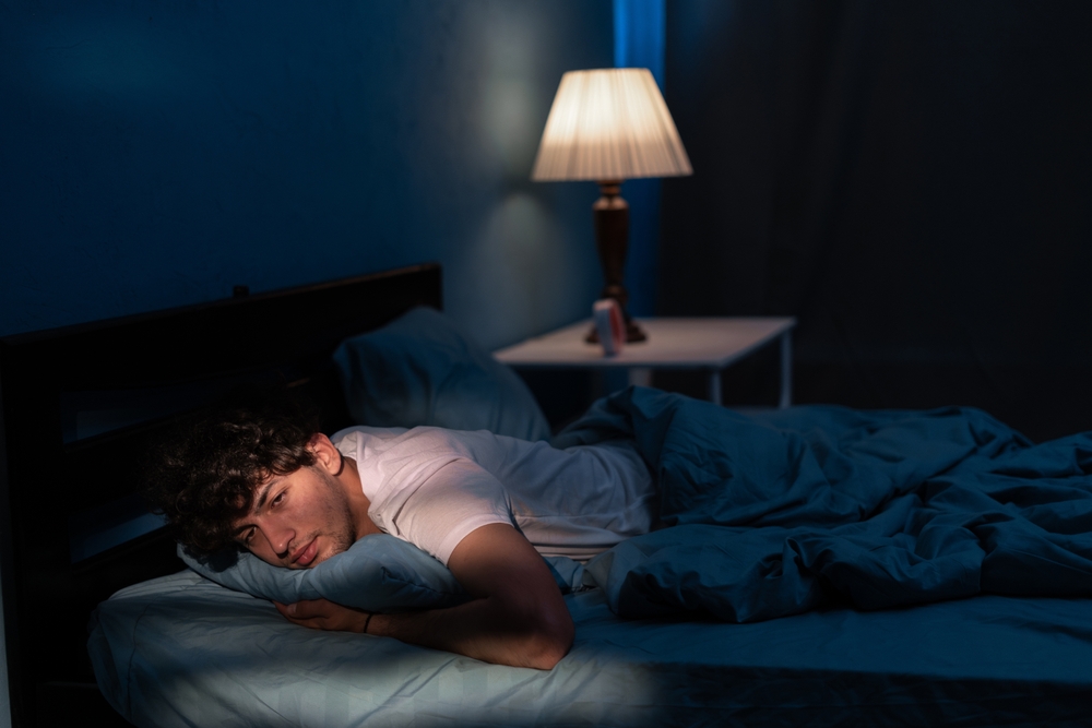 Arab man suffering from insomnia lying in bed with open eyes. Handsome guy in bed sleep disorder thinking about problems at night. Copy space