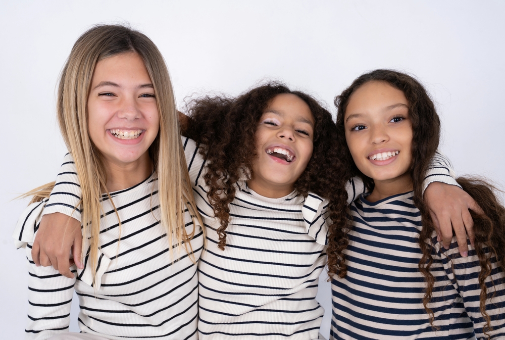 Three young multiracial kid girls hugging each other, having good time and playing.