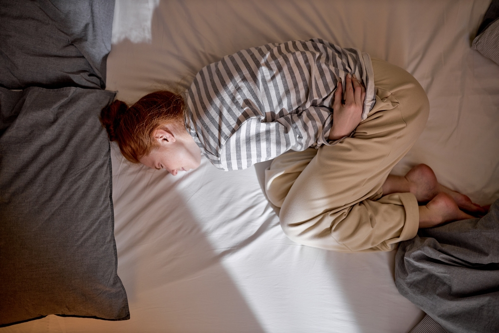 Top view of sick young ginger redhead woman lying in bed touch belly suffer from stomach ache, ill millennial girl struggle with periods pain, having eating disorder indigestion trouble top view