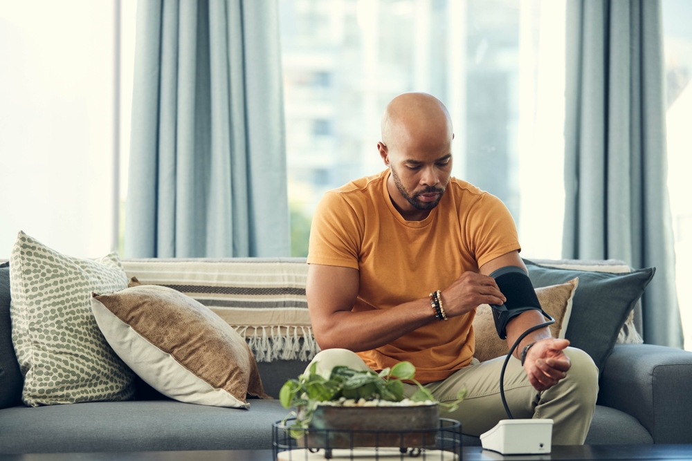 Im experiencing headaches so my blood pressure might be high. Shot of a young man taking his blood pressure while sitting on the sofa at home.
