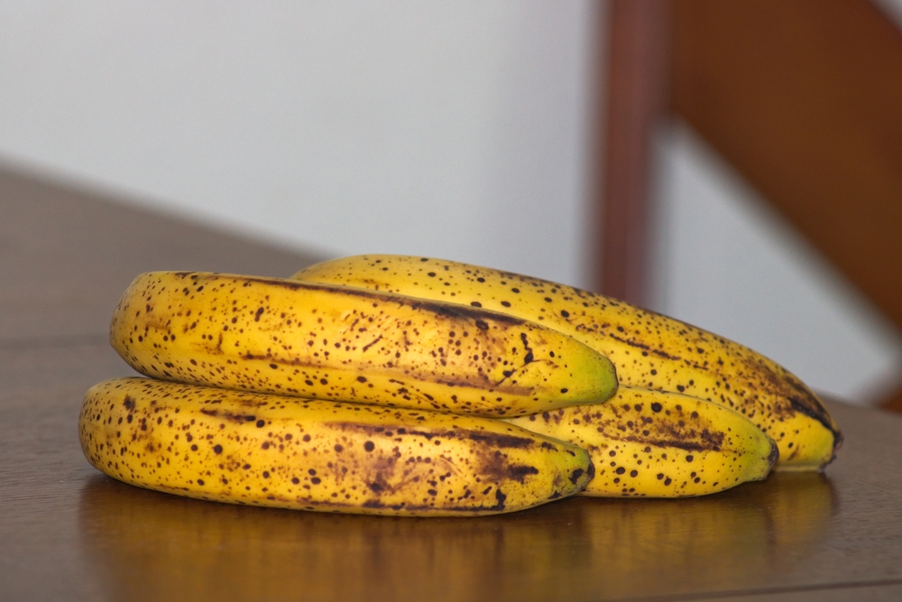 This is a photo shot of a ripe banana bunch with dark spots on table.