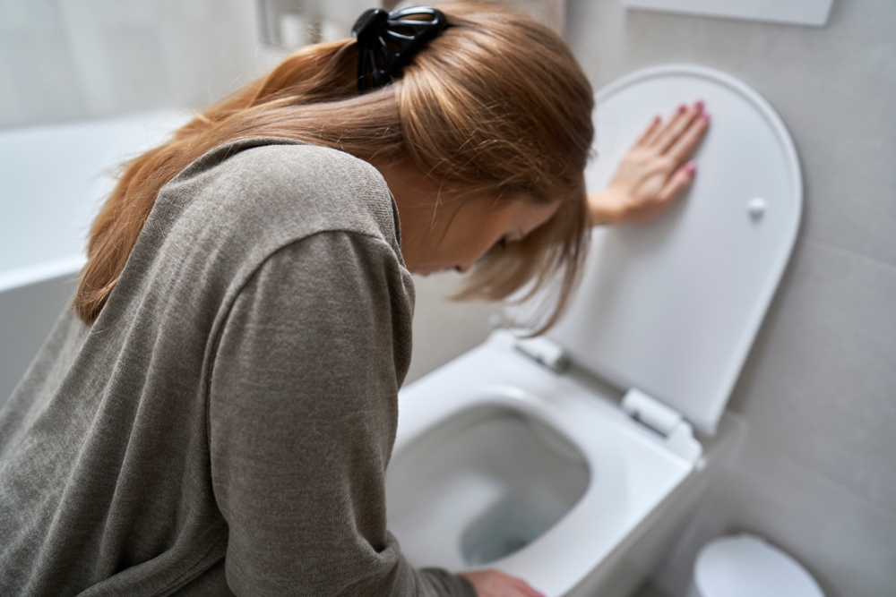 Woman bending over toilet and having a nausea