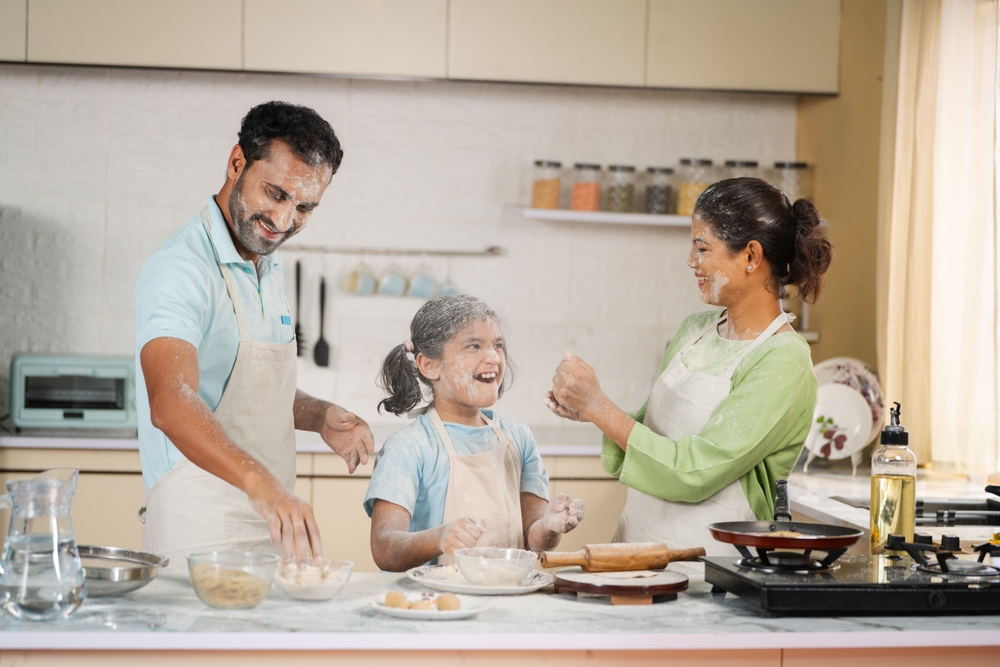 Playful Indian family with daughter plying flour while cooking at kitchen - concept of having fun, weekend holidays and relationship bonding
