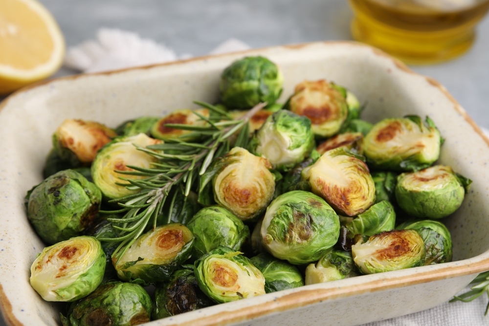Delicious roasted Brussels sprouts and rosemary in baking dish on table, closeup