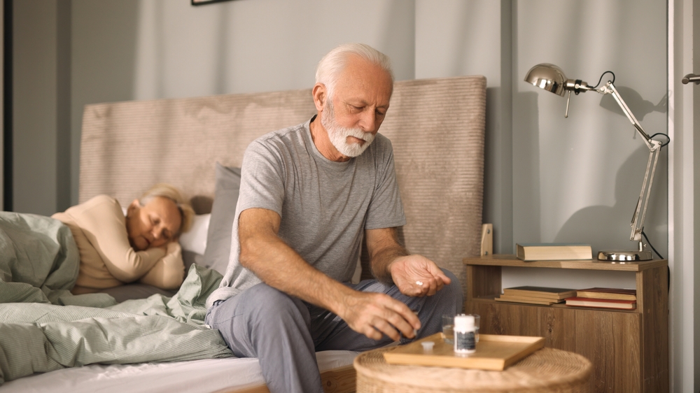 Elderly man taking medication with water in bedroom