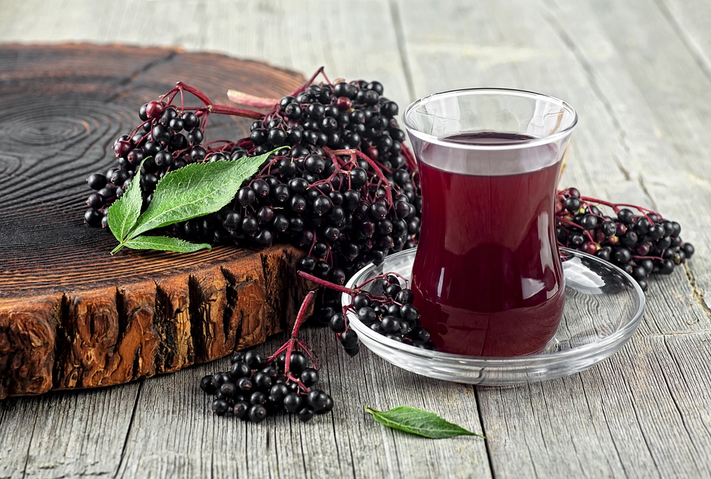 Fresh ripe black elderberries, elderberry syrup and leaves of elderberry on rustic wooden board. Alternative medicine and lifestyle.
