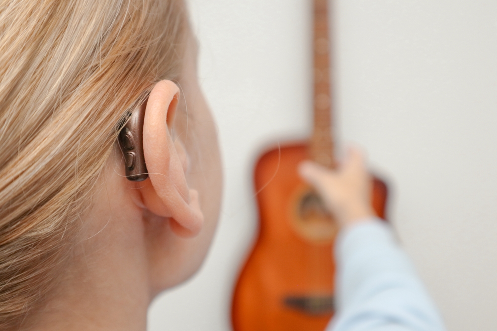 A woman with hearing loss can hear and play guitar again using a hearing aid. Adult woman with hearing aid behind the ear can hear sounds.
