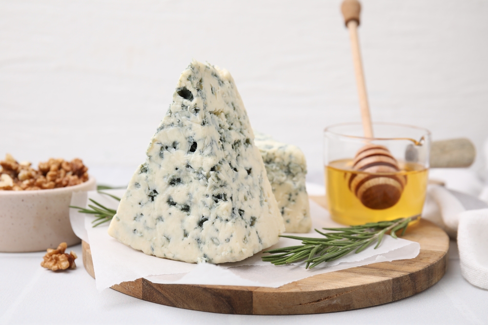 Tasty blue cheese with rosemary, honey and walnuts on white table
