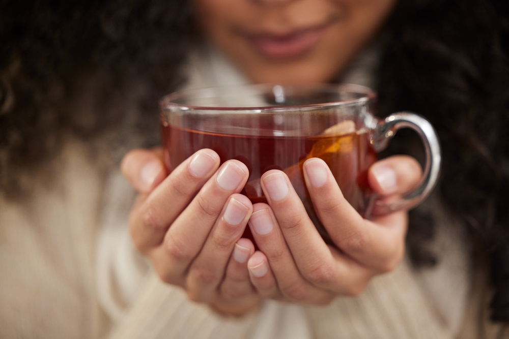 Person, hands and tea cup for winter drink with warm clothes for cozy weekend, relax or comfortable. Fingers, beverage and jersey for resting break or home peace for morning calm, health or herbal
